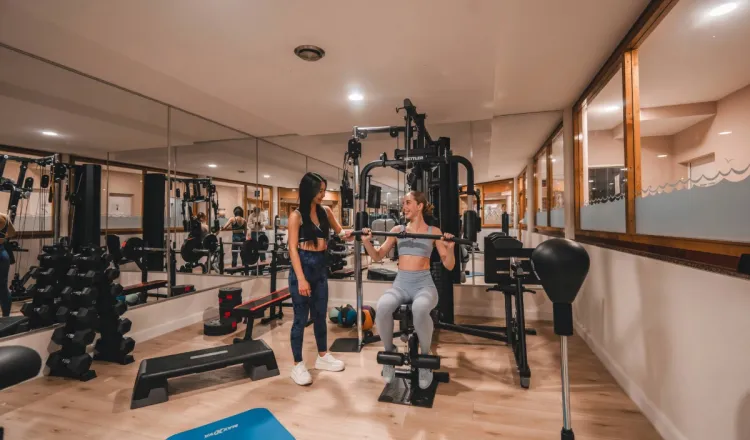 Zwei Damen trainieren im Fitnessraum des Arkona Strandhotels Binz auf Rügen mit Kraftgeräten, Hanteln und Spiegeln