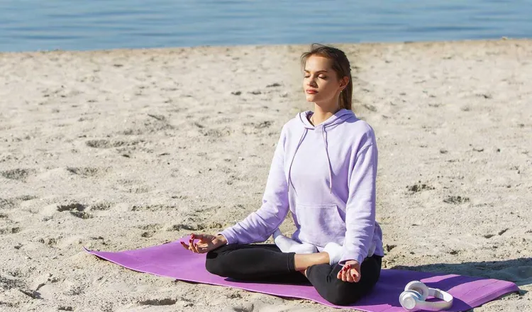 Frau meditiert beim Yoga am Strand auf Rügen mit der Ostsee im Hintergrund im Urlaub im Arkona Strandhotel in Binz.