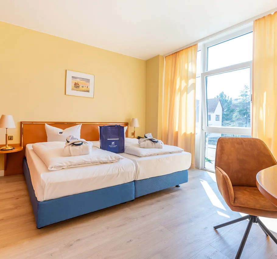 Helles Doppelzimmer in einer Suite geeignet als Familienzimmer an der Ostsee mit großen Fenstern, Doppelbett und bequemen Sesseln.