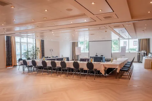 Tagungsraum mit U-förmiger Bestuhlung, Beamer-Leinwand, großen Fenstern und moderner Beleuchtung im Arkona Strandhotel in Binz.