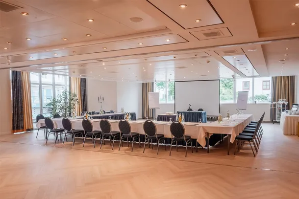 Tagungsraum mit U-förmiger Bestuhlung, Beamer-Leinwand, großen Fenstern und moderner Beleuchtung im Arkona Strandhotel in Binz.