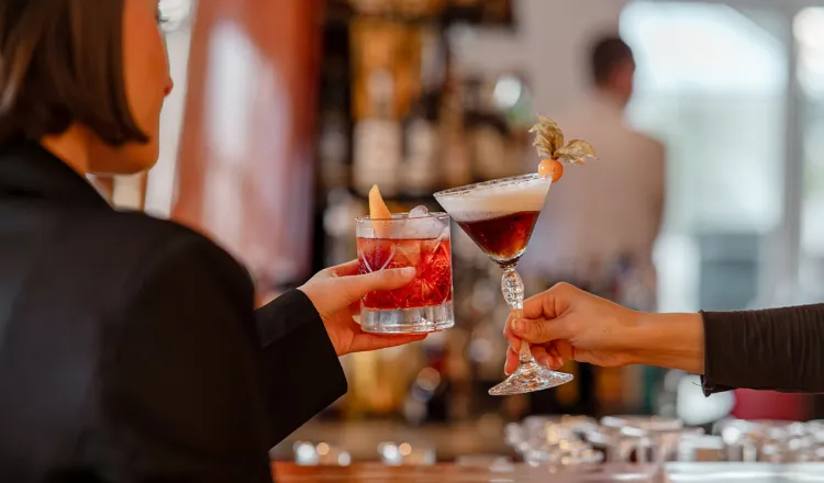 Gäste stoßen mit Cocktails am Bartresen von der Arkona Bar in Binz auf Rügen an.
