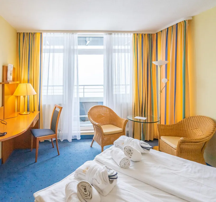 Doppelzimmer im Arkona Strandhotel Binz mit gemütlicher Sitzecke, Schreibtisch und Zugang zum Balkon mit Meerblick auf die Ostsee.