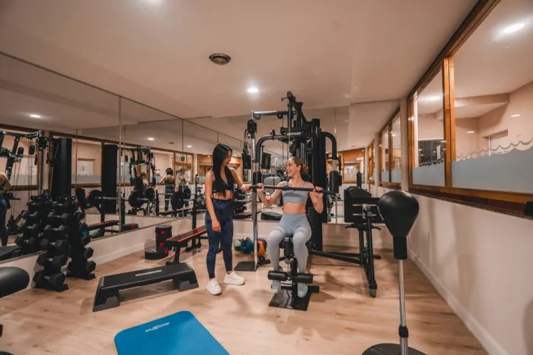 Zwei Damen trainieren im Fitnessraum des Arkona Strandhotels Binz auf Rügen mit Kraftgeräten, Hanteln und Spiegeln