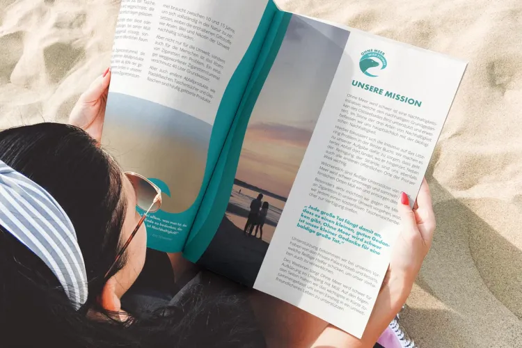 Frau liest das OMWS-Magazin am Strand von Binz – Arkona Strandhotel engagiert sich mit der Initiative „Ohne Meer wird schwer“ für Umweltschutz