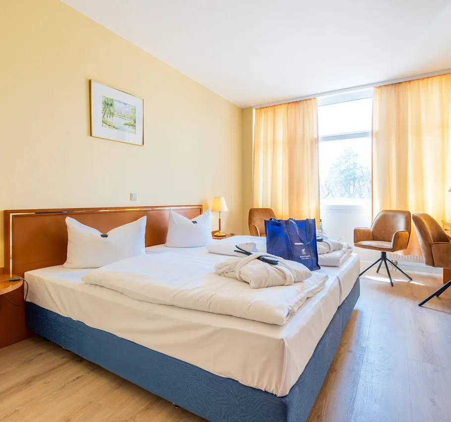 Doppelzimmer geeignet als Familienzimmer an der Ostsee mit Blick auf das Bett, eine Sitzecke und ein großes Fenster mit Stadtblick.