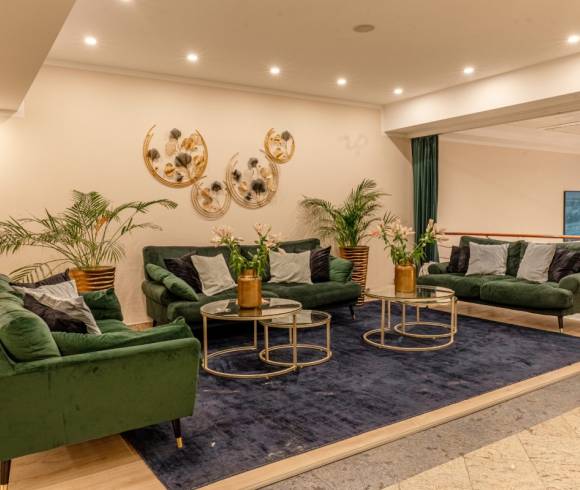 Der Innenbereich mit 3 grünen komfortablen Sofas, Pflanzen Dekos sowie Wanddeko Elemente im Arkona Strandhotel.
