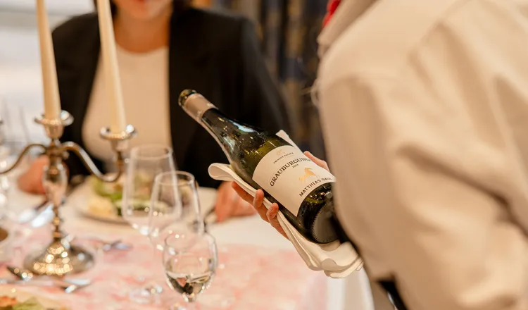 Kellner schenkt Grauburgunder Wein in Weinglas an sorgfältig dekorierten Tisch im Bar und Restaurant Rossini in Binz.