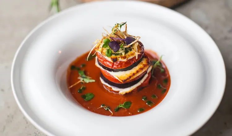 Ein aufwändig geschichtetes Ratatouille in einem weißen Teller, verziert mit Kräutern bei einem Bankett im Arkona Strandhotel auf Rügen.