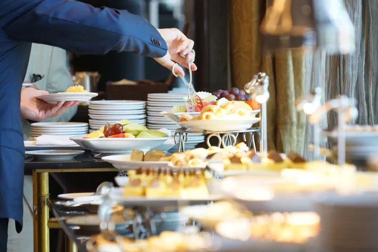 Ein Gast bedient sich am reichlich ausgestatteten Frühstücksbuffet mit Obst und Gebäck.