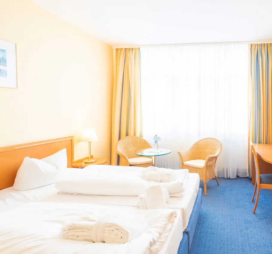 Doppelzimmer im Erdgeschoss geeignet als Familienzimmer an der Ostsee mit Blick auf das Bett, Sitzgelegenheit und Fenster mit Vorhängen.