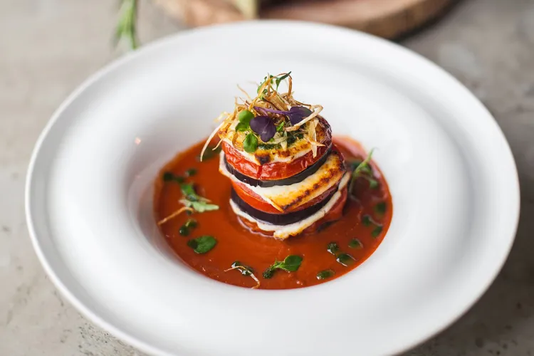 Ein aufwändig geschichtetes Ratatouille in einem weißen Teller, verziert mit Kräutern bei einem Bankett im Arkona Strandhotel auf Rügen.