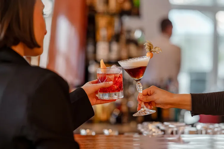 Gäste stoßen mit Cocktails am Bartresen von der Arkona Bar in Binz auf Rügen an.