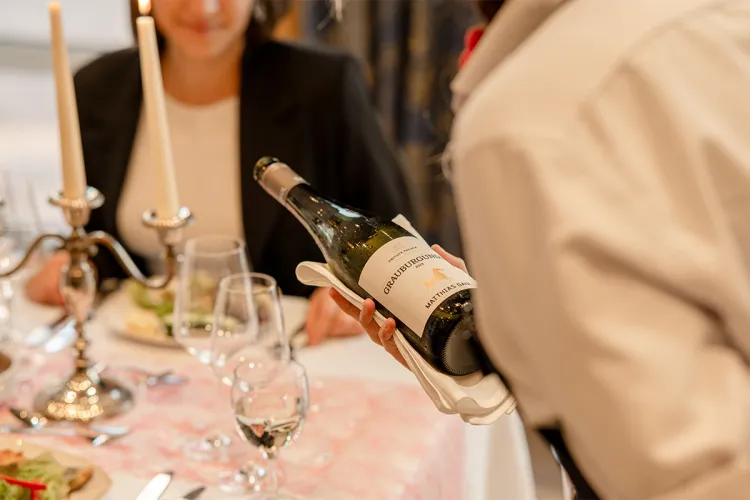 Kellner schenkt Grauburgunder Wein in Weinglas an sorgfältig dekorierten Tisch im Bar und Restaurant Rossini in Binz.