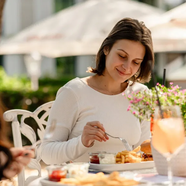 Frau genießt bei Sonnenschein ein Mittagessen mit Pommes, Burger und Getränk im Freien bei einem Wellnessangbeot auf Rügen.