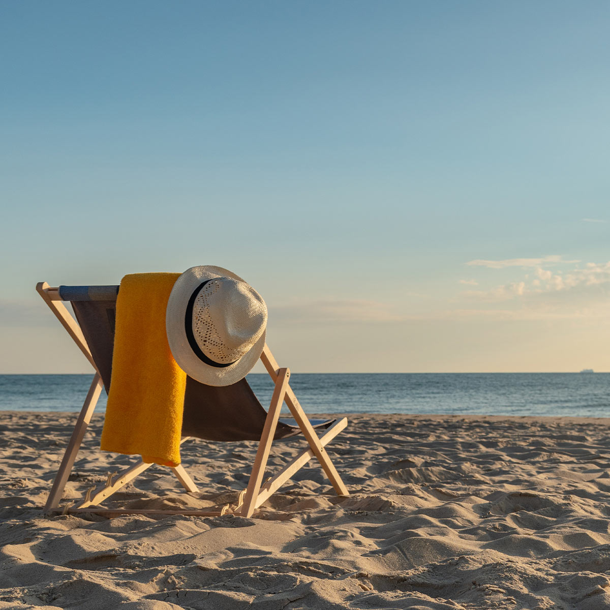 Ein gemütlicher Liegestuhl mit einem Sonnenhut und einem Handtuch am Ostseestrand in Binz bei sonnigem Wetter.