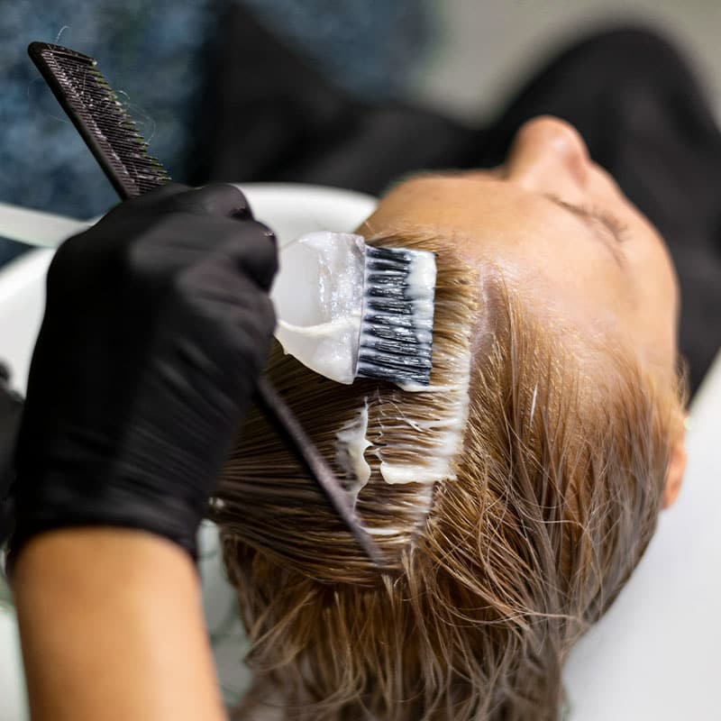 Auftrag neuer Haarfarbe mit dem Pinsel auf dem Haar einer Kundin.