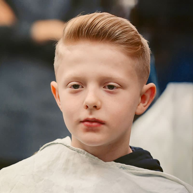 Ein blonder Junge mit Kleiderschutz, neuem Kurzhaarschnitt und Styling.