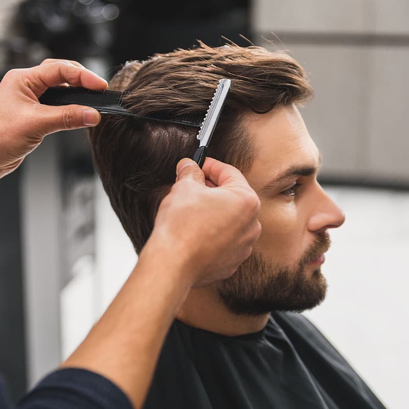 Dunkelblonder Mann erhält lockere Kurzhaarfrisur mit Kamm und Rasiermesser.