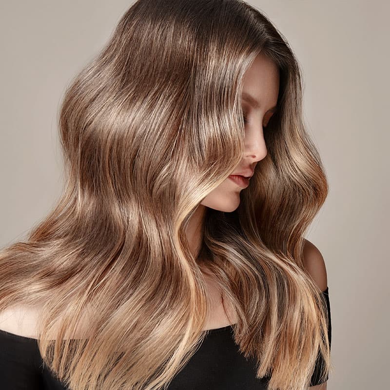 Eine voluminöse Wellenfrisur an den langen Haaren einer blonden Frau.