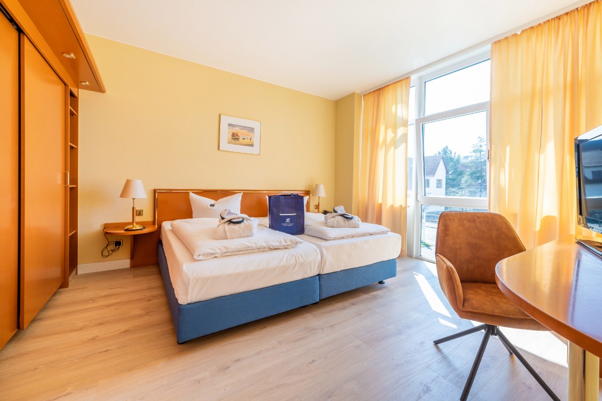 Eine helle, geräumige Suite mit Stadtblick im Arkona Strandhotel mit Doppelbett, Nachttischen, großem Schrank und Schreibtisch.