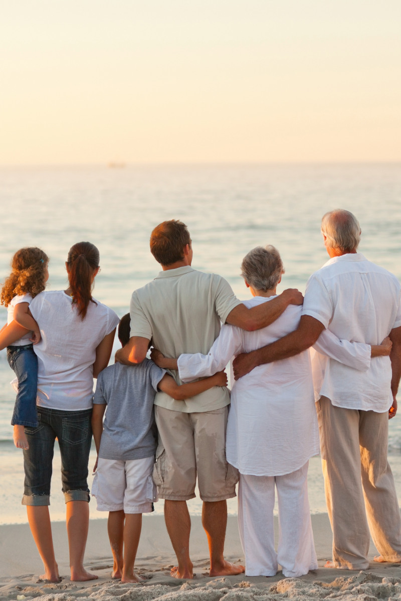 Eine Familie mit zwei Kindern, zwei Eltern sowie zwei Großeltern schaut sich gemeinsam am Ostseestrand den Sonnenuntergang an.